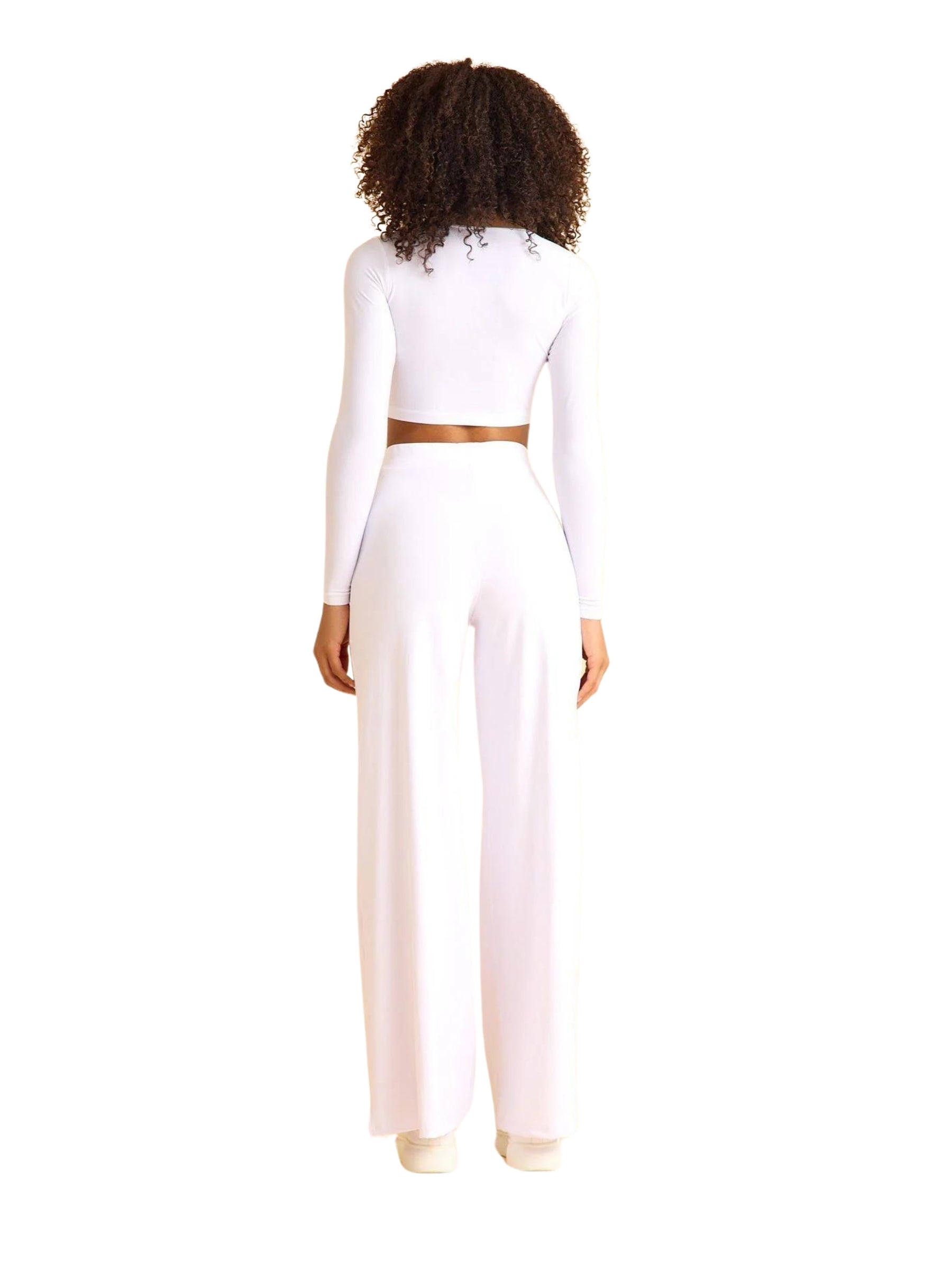 Person mit Locken in der 445 Mumbai Yoga Hose von Lismina, die ein weißes bauchfreies Top vor einem schlichten weißen Hintergrund trägt.